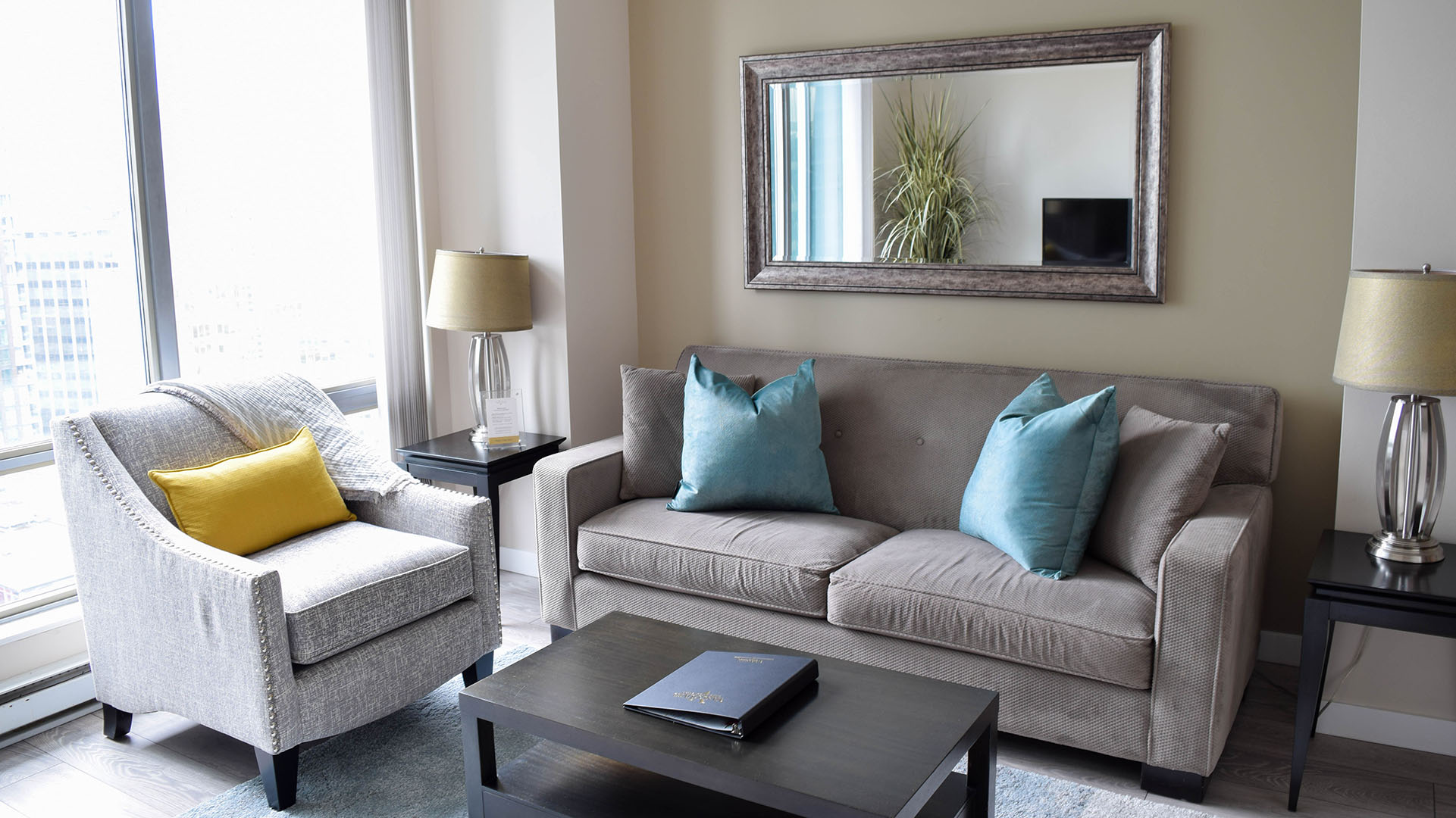 Grey sofa, light grey chair, and a wall mirror in the living room of apartment 1903-1200 West Georgia, at the Residences on Georgia.