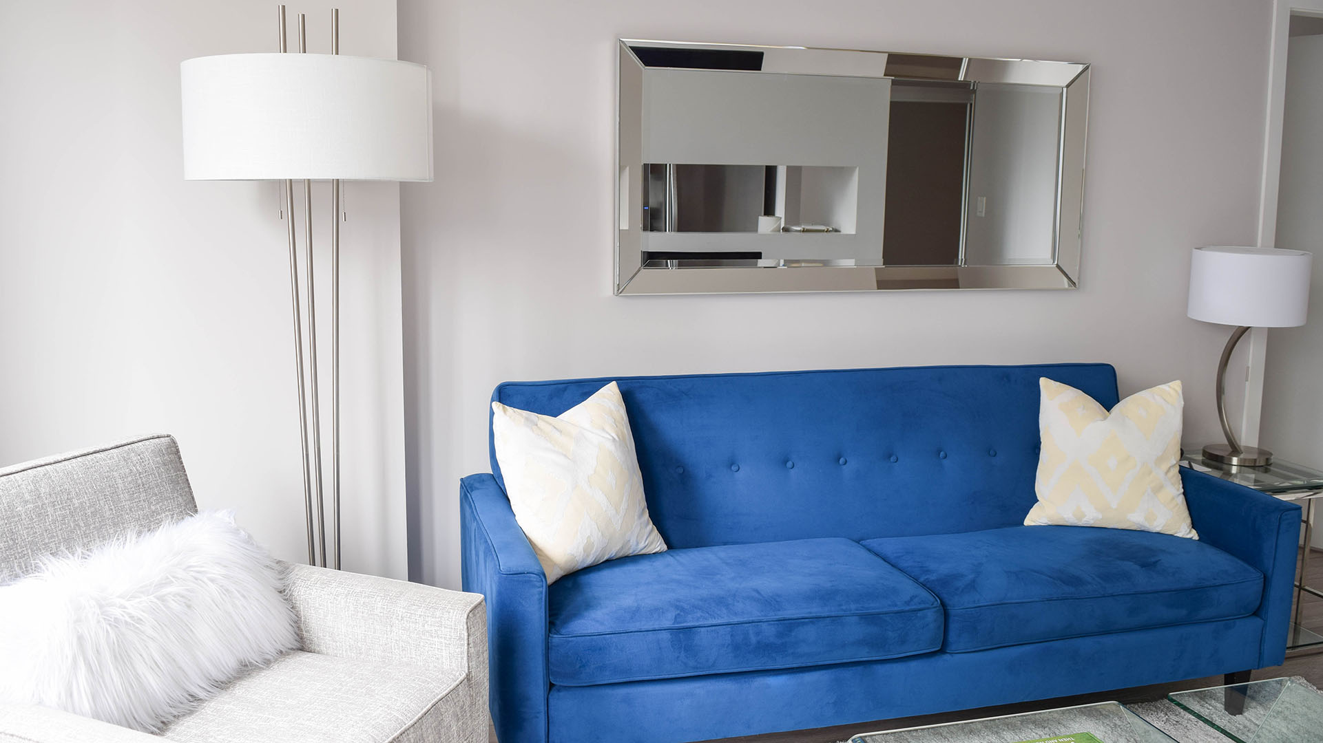 Blue sofa, light grey chair, and a wall mirror in the living room of apartment 302-1288 West Georgia, at the Residences on Georgia.