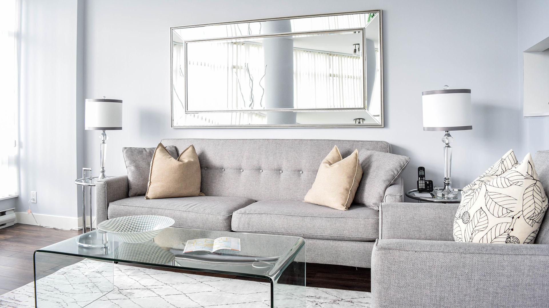Grey sofa, glass coffee table, and a wall mirror in the living room of apartment 902-1288 Alberni St. at the Palisades.