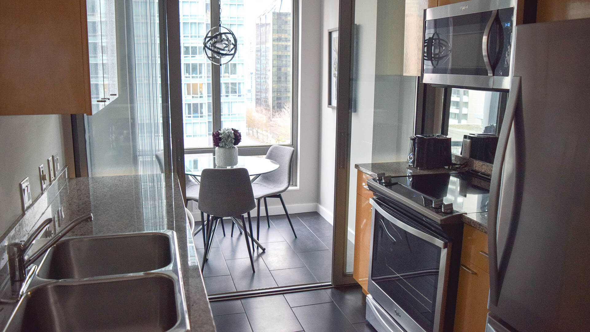 Modern kitchen with stainless steel appliances, granite countertop and dining table and chairs in the adjacent dining area in furnished apartment at Vancouver Extended Stay
