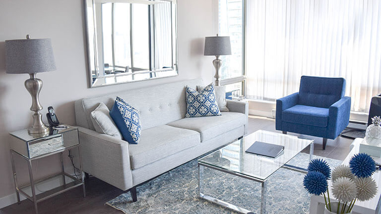 Living room with a light grey sofa, a blue chair and a glass coffee table in a move-in ready, fully furnished two bedroom apartment at Vancouver Extended Stay